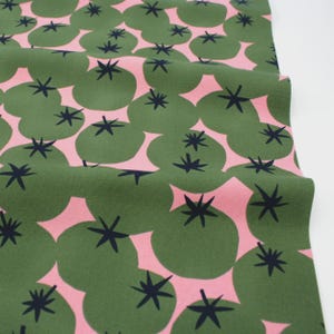 Könnte beinhalten: Grüner Stoff mit einem sich wiederholenden Muster aus stilisierten grünen Formen mit schwarzen Sternen auf einem rosa Hintergrund. Der Stoff ist gefaltet und zeigt die Textur und das Design. Das Thema ist ein botanischer oder naturnaher Textil.