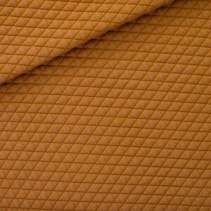 Peut inclure: Gros plan sur un tissu texturé de couleur brun doré chaud. Le matériau présente un motif de losanges matelassés, créant une texture visuellement attrayante. Le tissu est plié, montrant le dessous et ajoutant de la profondeur à l'image. Idéal pour l'habillement ou la décoration intérieure.