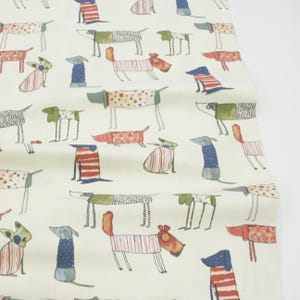 Könnte beinhalten: Cremefarbener Stoff mit einem sich wiederholenden Muster von illustrierten Hunden. Die Hunde sind in verschiedenen Posen und Outfits dargestellt, darunter gestreifte Hemden und gepunktete Mäntel. Die Farbgebung umfasst Rot, Blau, Grün und Orange.