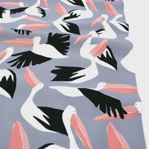 May include: A fabric featuring a repeating pattern of pelicans in white, black, and coral pink against a pale blue backdrop. The pelicans are depicted in a stylized manner, with wings extended or folded, and open beaks.