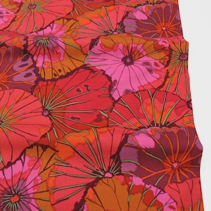 Könnte beinhalten: Nahaufnahme eines Stoffes mit einem sich wiederholenden Blumenmuster. Das Design zeigt große, stilisierte Blumen in Rot-, Orange- und Rosatönen mit grünen Akzenten. Der Stoff hat eine glatte Textur und ein lebendiges Aussehen.