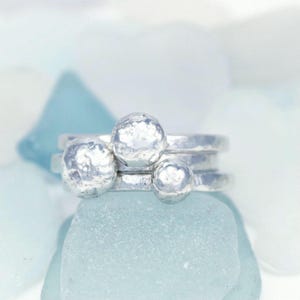 May include: A set of three silver rings with textured, round, bubble-like details. The rings are stacked on top of each other.