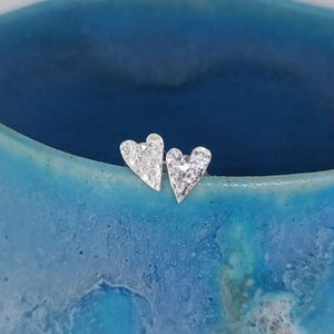 May include: A pair of silver heart-shaped stud earrings with a textured surface.