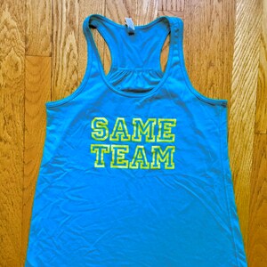 May include: A light blue tank top with a yellow and green graphic that says "SAME TEAM".