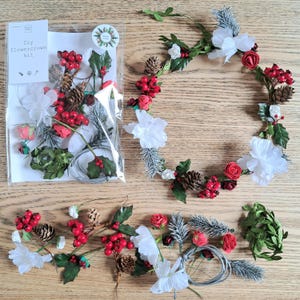 May include: A DIY flower crown kit with components for crafting. The kit includes red berries, white flowers, pine cones, and green foliage. A finished flower crown is displayed, showcasing the assembled elements. The kit also includes wire.