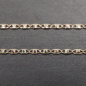 May include: Two gold chains with a patterned design. The chains are on a dark gray background.