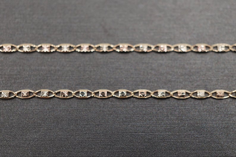 May include: Two gold chains with a patterned design. The chains are on a dark gray background.