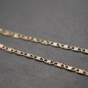 May include: A gold chain necklace with a delicate, patterned design. The chain is made of three different shades of gold, creating a unique and stylish look.