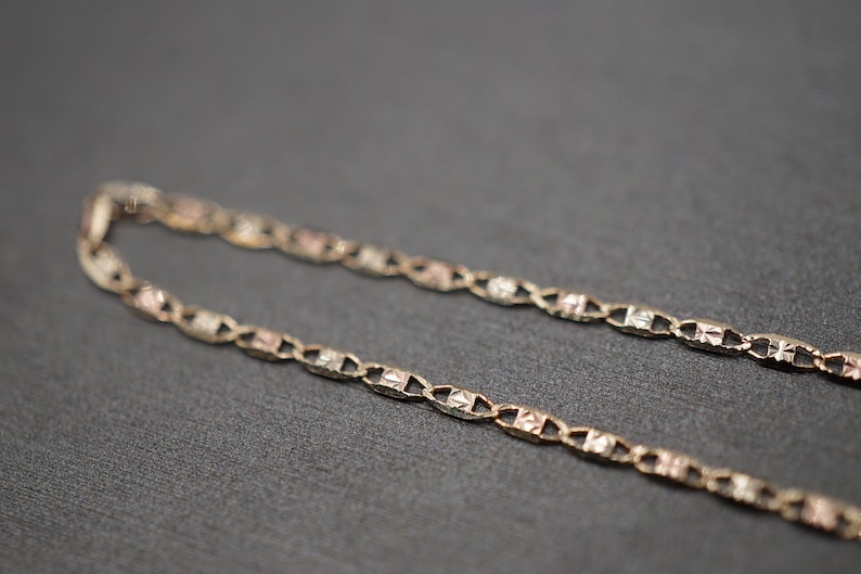 May include: A gold chain necklace with a delicate, patterned design. The chain is made of three different shades of gold, creating a unique and stylish look.