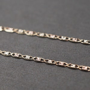 May include: A delicate gold chain necklace with a two-tone design. The chain is made of alternating links of yellow and rose gold.