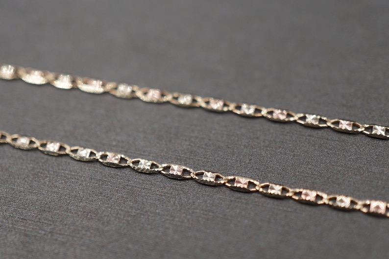 May include: A delicate gold chain necklace with a two-tone design. The chain is made of alternating links of yellow and rose gold.