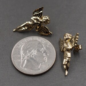 May include: Two gold-tone angel figurines. The angels are about the size of a quarter. One angel is holding a musical instrument.