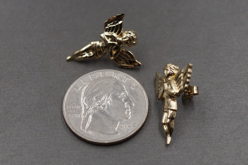 May include: Two gold-tone angel figurines. The angels are about the size of a quarter. One angel is holding a musical instrument.