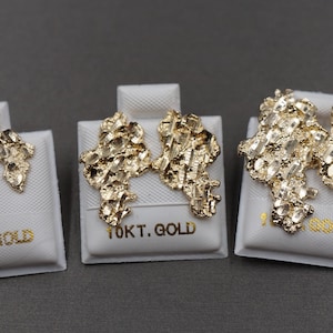 May include: Three pairs of gold nugget earrings displayed on white cards. The cards have the text "10KT. GOLD" printed on them.