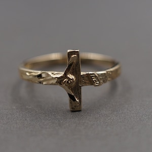 May include: A gold ring with a detailed cross design featuring a figure of Jesus Christ.