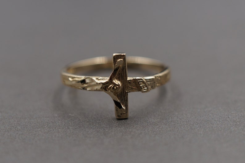 May include: A gold ring with a detailed cross design featuring a figure of Jesus Christ.
