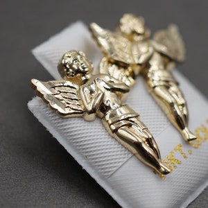 May include: A pair of gold angel earrings. The angels are depicted with wings and are facing each other. The earrings are on a white background with the text "14K GOLD" printed on it.