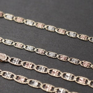 May include: Three gold chains with a tri-color design. The chains are made of yellow, white, and rose gold. The chains are linked together with a square-shaped link. The chains are on a black surface.
