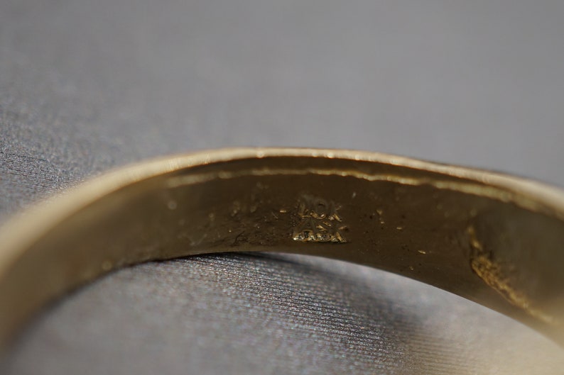 May include: Close-up of the inside of a gold band ring with the inscription "14K" and "Italy" visible.