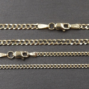 May include: Four gold chains of different lengths and widths. The chains are all made of a curb link style. The chains are laid out in a row on a gray surface.