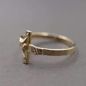 May include: A gold-toned ring with a detailed cross design. The ring is simple and elegant.