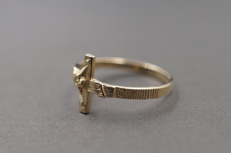 May include: A gold-toned ring with a detailed cross design. The ring is simple and elegant.