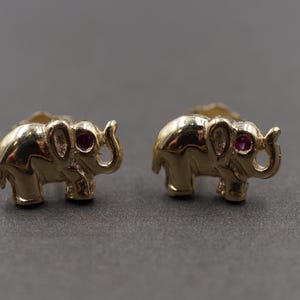 May include: A pair of gold elephant stud earrings with red gemstone accents.