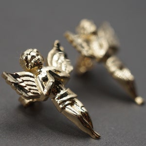 May include: A pair of gold-tone angel earrings. Each earring features a detailed angel figure with wings.