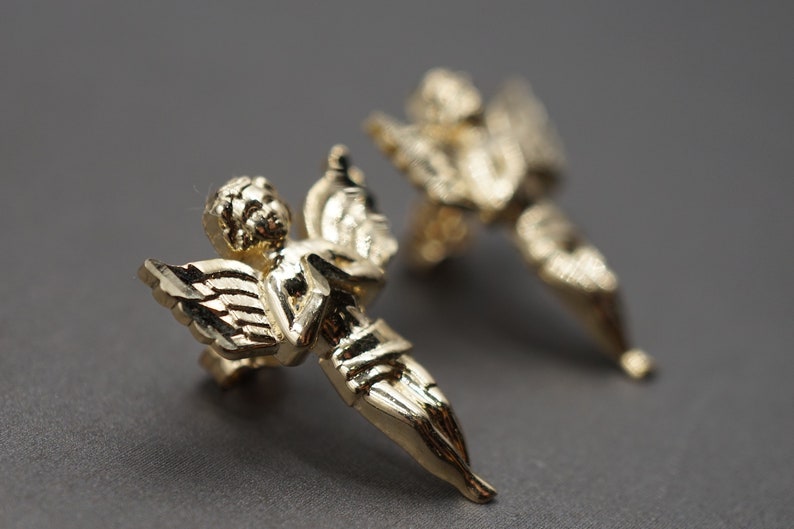 May include: A pair of gold-tone angel earrings. Each earring features a detailed angel figure with wings.