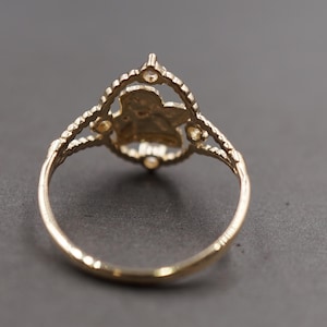 May include: A gold ring featuring a central openwork design shaped like a flower or star, framed by a scalloped border with small circular accents. The band is thin and smooth, connecting to the decorative top section with a split shank structure.