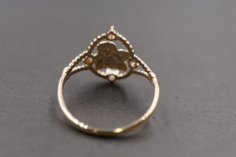 May include: A gold ring featuring a central openwork design shaped like a flower or star, framed by a scalloped border with small circular accents. The band is thin and smooth, connecting to the decorative top section with a split shank structure.