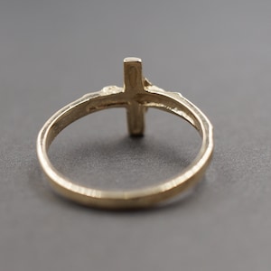 May include: A gold-toned ring with a cross design. The ring is simple and elegant.