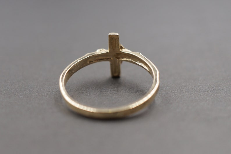 May include: A gold-toned ring with a cross design. The ring is simple and elegant.