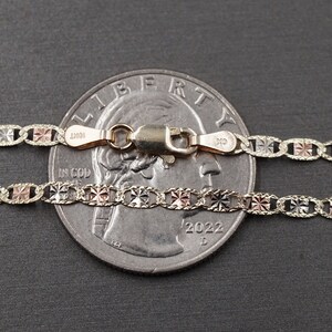 May include: Two gold chains with a diamond-shaped pattern, one is white gold, the other is rose gold, both are laid out on a gray surface next to a US quarter.
