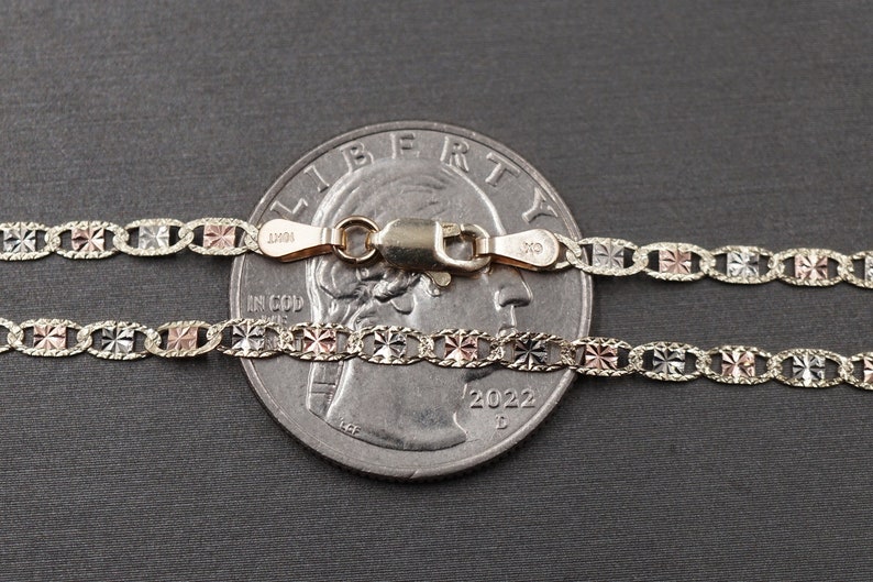 May include: Two gold chains with a diamond-shaped pattern, one is white gold, the other is rose gold, both are laid out on a gray surface next to a US quarter.