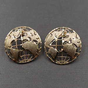 May include: A pair of gold-tone earrings featuring a globe design. The globe is textured and has a wire-like outline.