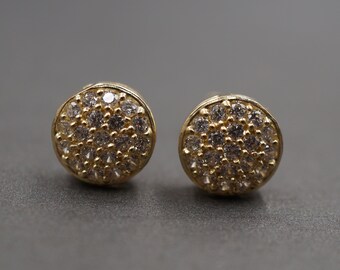 May include: A pair of gold stud earrings with a round design. Each earring is covered in small, clear stones.