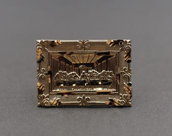May include: A gold-toned pendant featuring a detailed depiction of the Last Supper within a decorative frame.