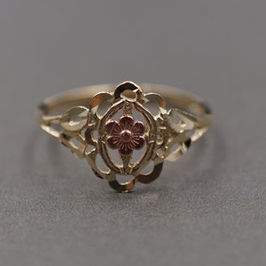 May include: A gold ring with a delicate filigree design and a rose-colored flower in the center.