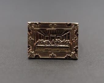 May include: A gold-toned ring with an ornate frame depicting the Last Supper. The ring features intricate details and a raised design.