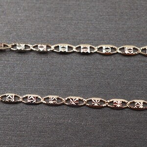 May include: Two gold chains with a patterned design. The chains are made of oval links with a diamond-shaped pattern.