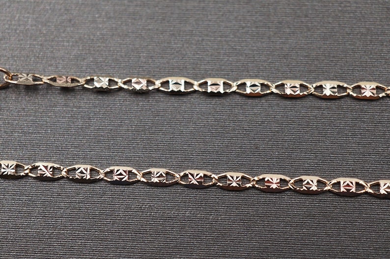 May include: Two gold chains with a patterned design. The chains are made of oval links with a diamond-shaped pattern.