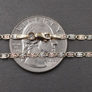 May include: A tri-color gold chain necklace with a lobster clasp. The chain is made of yellow, white, and rose gold and features a cross design. The chain is laid out on top of a US quarter dollar coin for size reference.