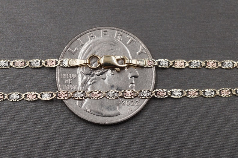 May include: A tri-color gold chain necklace with a lobster clasp. The chain is made of yellow, white, and rose gold and features a cross design. The chain is laid out on top of a US quarter dollar coin for size reference.