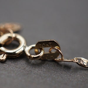 May include: Close-up of a gold chain necklace clasp with a 10KT marking. The chain is a delicate, patterned design.