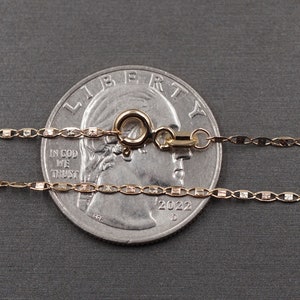 May include: Two gold chains with a lobster clasp, laid out on top of a US quarter dollar coin. The coin is dated 2022.