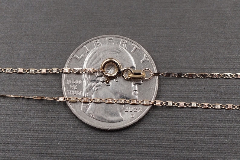 May include: Two gold chains with a lobster clasp, laid out on top of a US quarter dollar coin. The coin is dated 2022.
