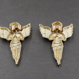 May include: A pair of gold angel wing earrings with a detailed design. The earrings are made of metal and have a post back closure.