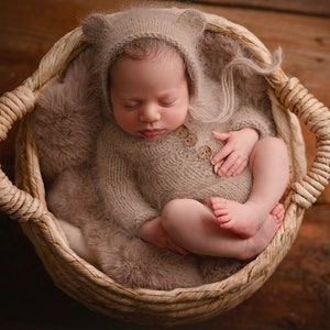 Könnte beinhalten: Ein neugeborenes Baby in einem gestrickten braunen Outfit mit passender Mütze, das in einem geflochtenen Korb schläft.