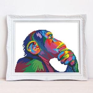 Può includere: Uno schema di punto croce colorato di uno scimpanzé con il mento appoggiato sulla mano, che guarda pensieroso di lato.